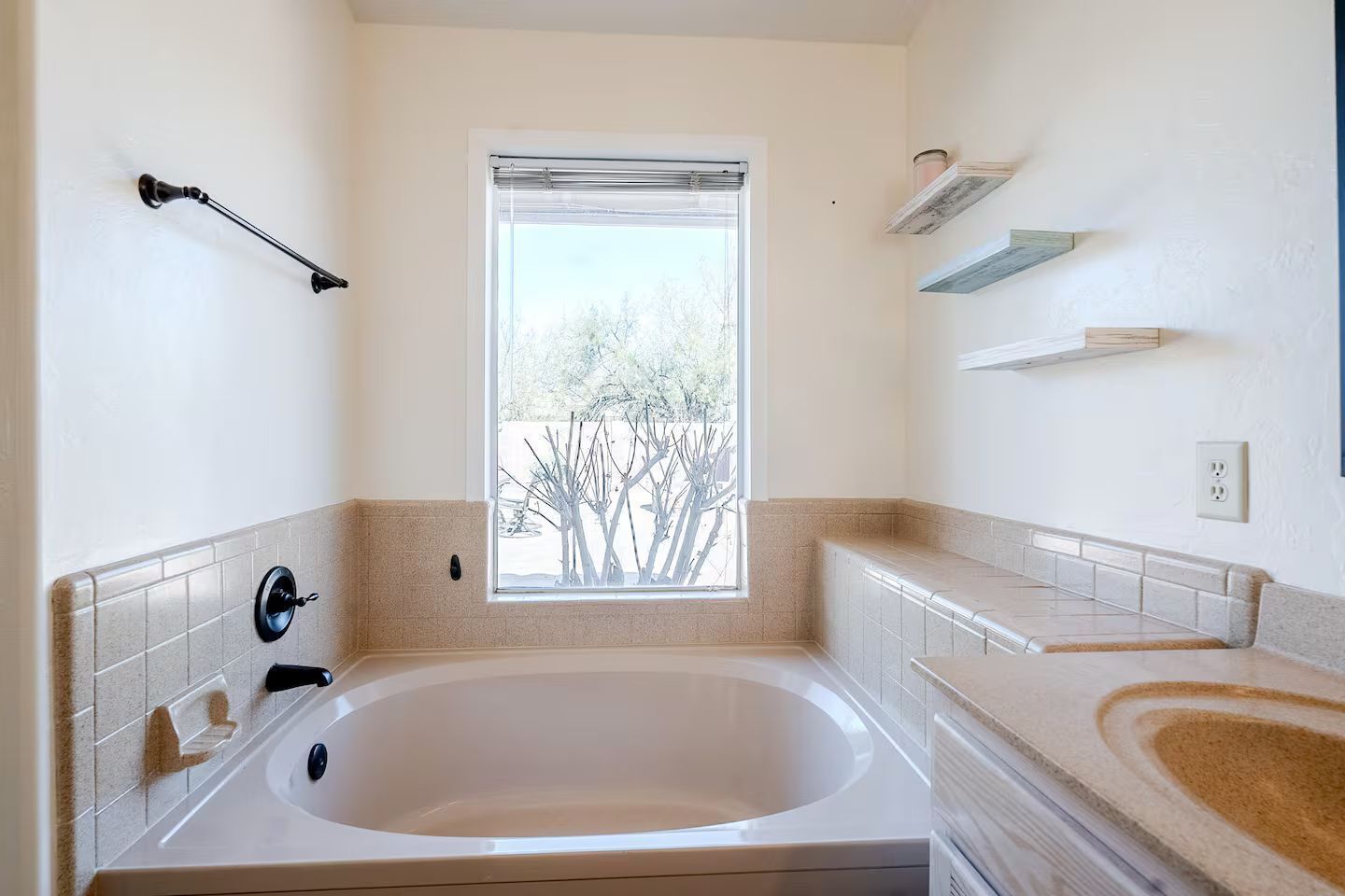 A modern bathroom with a large bathtub, a window with a view of trees, and a tiled backsplash.