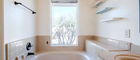 A modern bathroom with a large bathtub, a window with a view of trees, and a tiled backsplash.