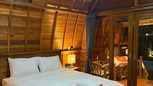 A cozy wooden cabin room with a bed, a nightstand, and a table with chairs. - Qchen Cuan Cabin Amed  (Karangasem)