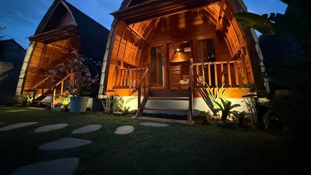 A wooden cabin with a porch and steps leading to the entrance, surrounded by potted plants and a stone pathway. - Qchen Cuan Cabin Amed  (Karangasem)