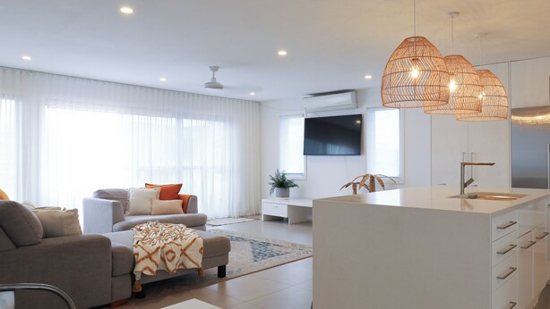 A modern living room with a sofa, a coffee table, and a TV. There is a kitchen area with a sink and a dining table. - CASA DEL MAYA - 2-Bed Home By the Sea | Water Views | Air Con | Wifi | Sauna (Anna Bay)