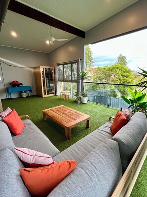 En moderne stue med sofa, sofabord i træ og balkon med udsigt over landskabet.