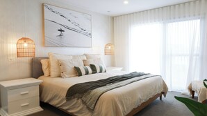 A bedroom with a large bed, two bedside tables, a wall-mounted artwork, and two wall-mounted lamps. - CASA DEL MAYA - 2-Bed Home By the Sea | Water Views | Air Con | Wifi | Sauna (Anna Bay)