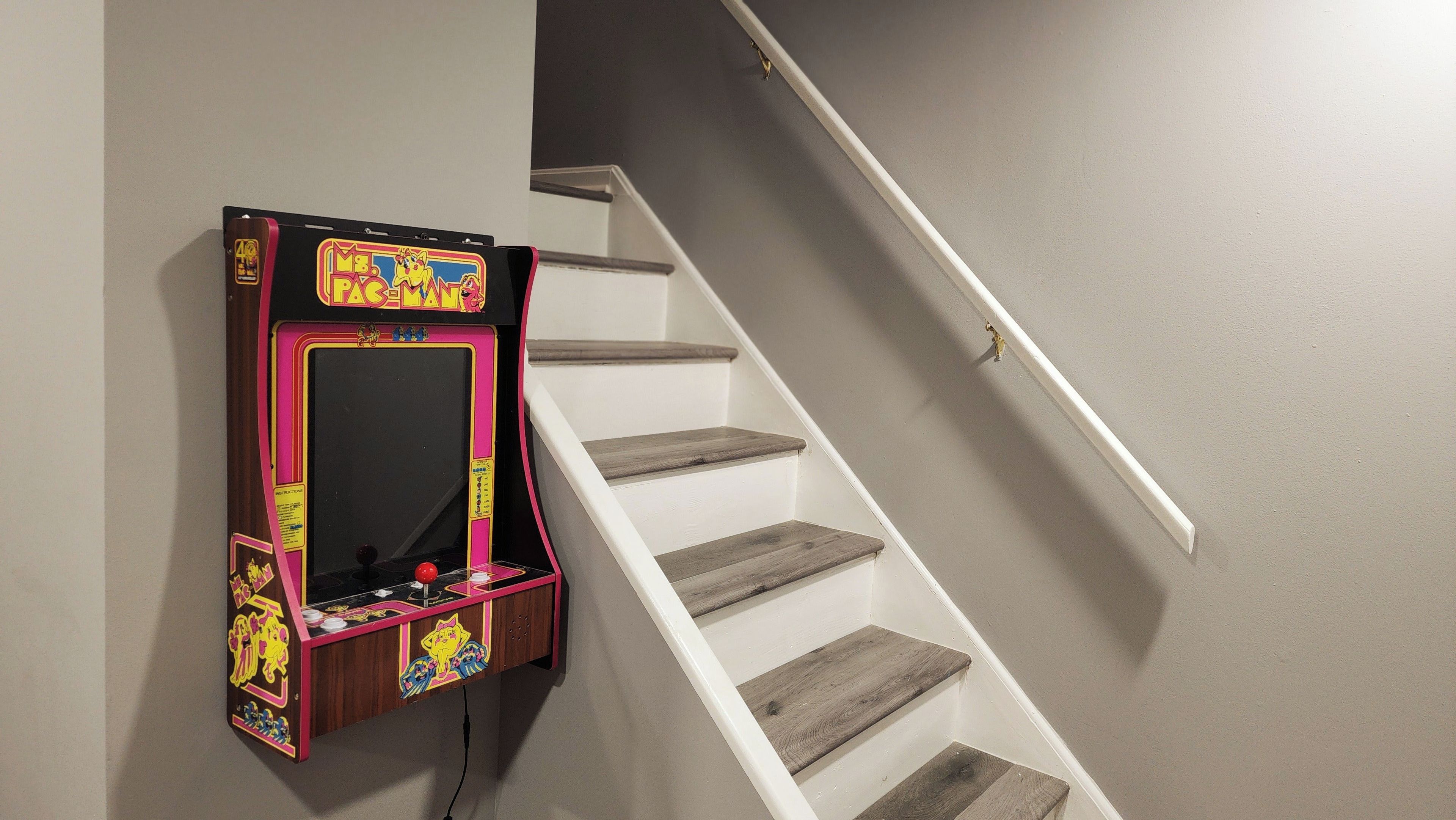 Eine Treppe mit einem an der Wand befestigten Pac-Man-Spielautomaten.