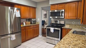 A kitchen with stainless steel appliances, wooden cabinets, granite countertops, and a tiled floor. - Spacious 5-bedroom house in charming Parkville with Hot tub 24/7 (Parkville)