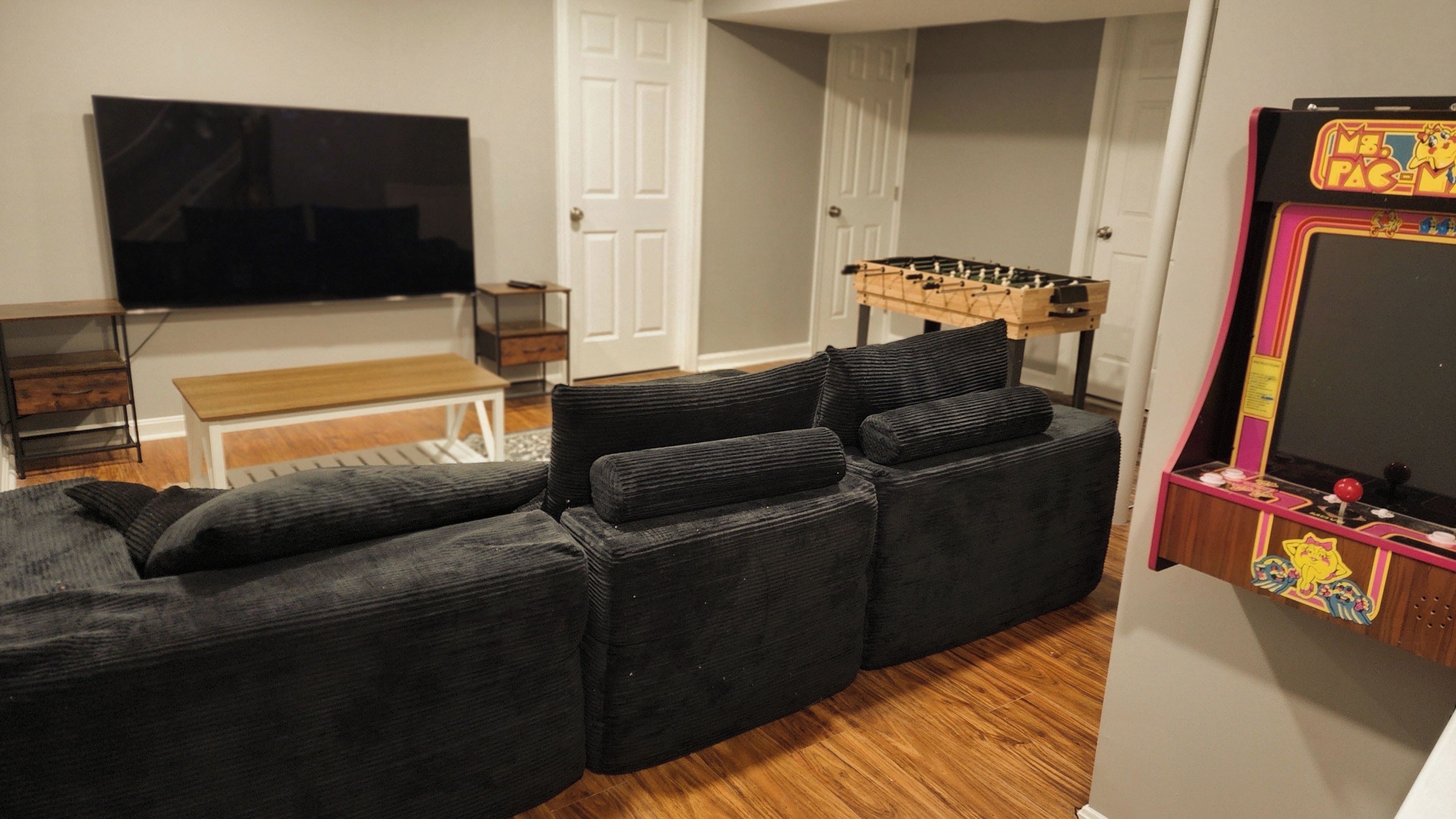 A living room with a sectional sofa, a foosball table, a television, and a bench.