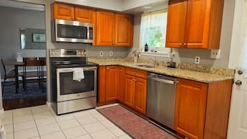 A kitchen with wooden cabinets, stainless steel appliances, a granite countertop, and a tiled floor.