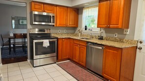 Una cocina con armarios de madera, electrodomésticos de acero inoxidable, encimera de granito y suelo de baldosas.