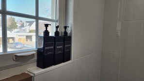 Three black bottles of body wash, shampoo, and conditioner on a white shelf by a window.