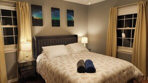 A hotel room with a bed, two bedside lamps, a nightstand, and three framed pictures on the wall. - Spacious 5-bedroom house in charming Parkville with Hot tub 24/7 (Parkville)