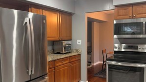 A modern kitchen with stainless steel appliances, wooden cabinets, and a tiled floor. - Spacious 5-bedroom house in charming Parkville with Hot tub 24/7 (Parkville)