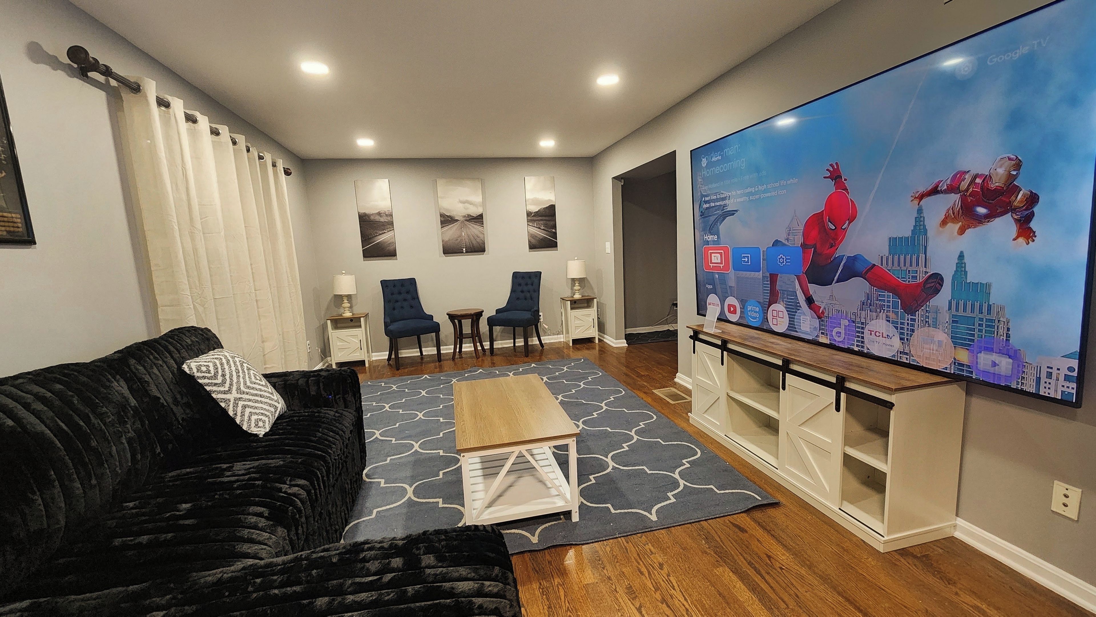 A living room with a black sofa, a coffee table, a flat-screen TV, and two chairs.