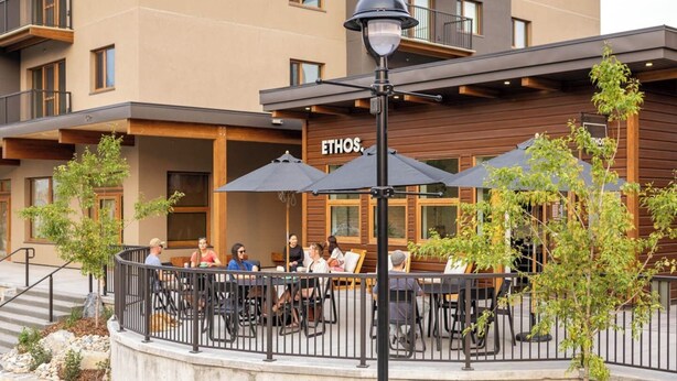 An outdoor seating area with tables and chairs, a wooden building with the name "ETHOS" visible, and a street lamp. - Casa del Oso - DT Condo, River & Mountain Views (Golden)