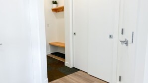 A hallway with a wooden floor, white walls, and a white door at the end. There is a shelf with a plant and hooks on the wall. - Casa del Oso - DT Condo, River & Mountain Views (Golden)