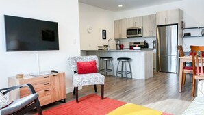 A modern living room with a TV, a sofa, a red rug, and a yellow ottoman. - Casa del Oso - DT Condo, River & Mountain Views (Golden)