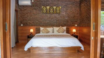Un dormitorio con pared de ladrillo, una cama con ropa blanca, dos mesitas de noche con lámparas y una ventana con cortinas.