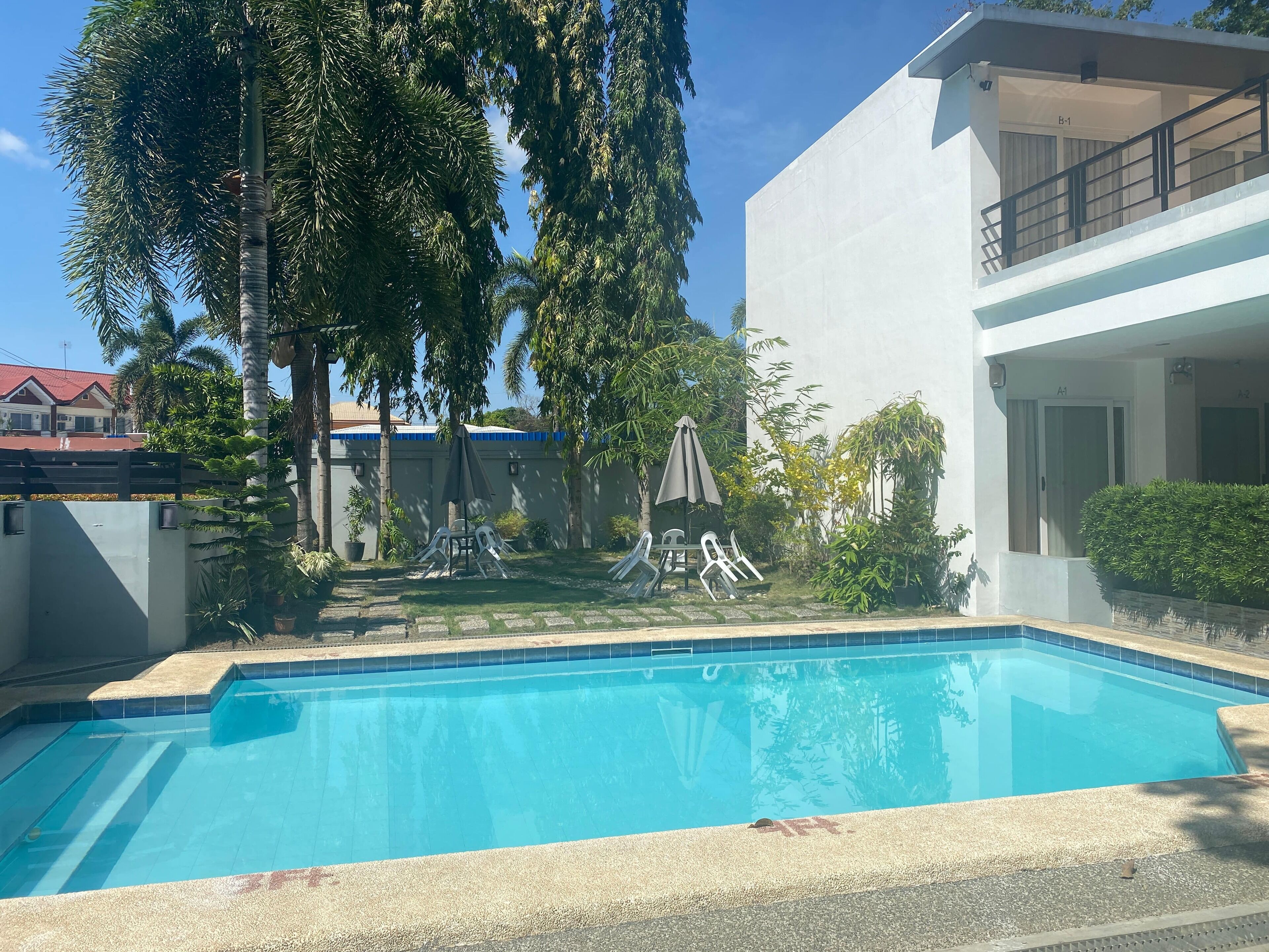 Una piscina con acqua cristallina, circondata da un giardino con alberi e un edificio moderno.