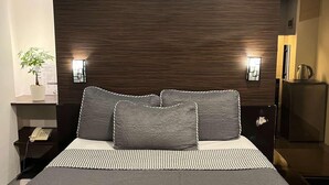 A modern bedroom with a large bed, dark wood headboard, bedside tables, a nightstand, a telephone, and a small potted plant.