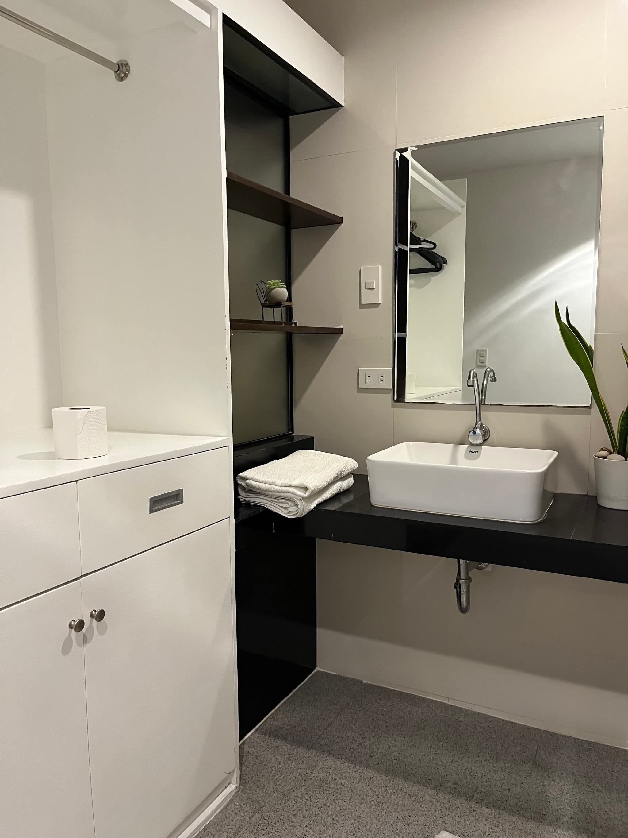 A modern bathroom with a white vanity, black shelves, a large mirror, and a white sink.