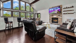 A spacious living room with a fireplace, large windows, and leather furniture. - Lakefront Home in the Poconos with Hot Tub! (Albrightsville)