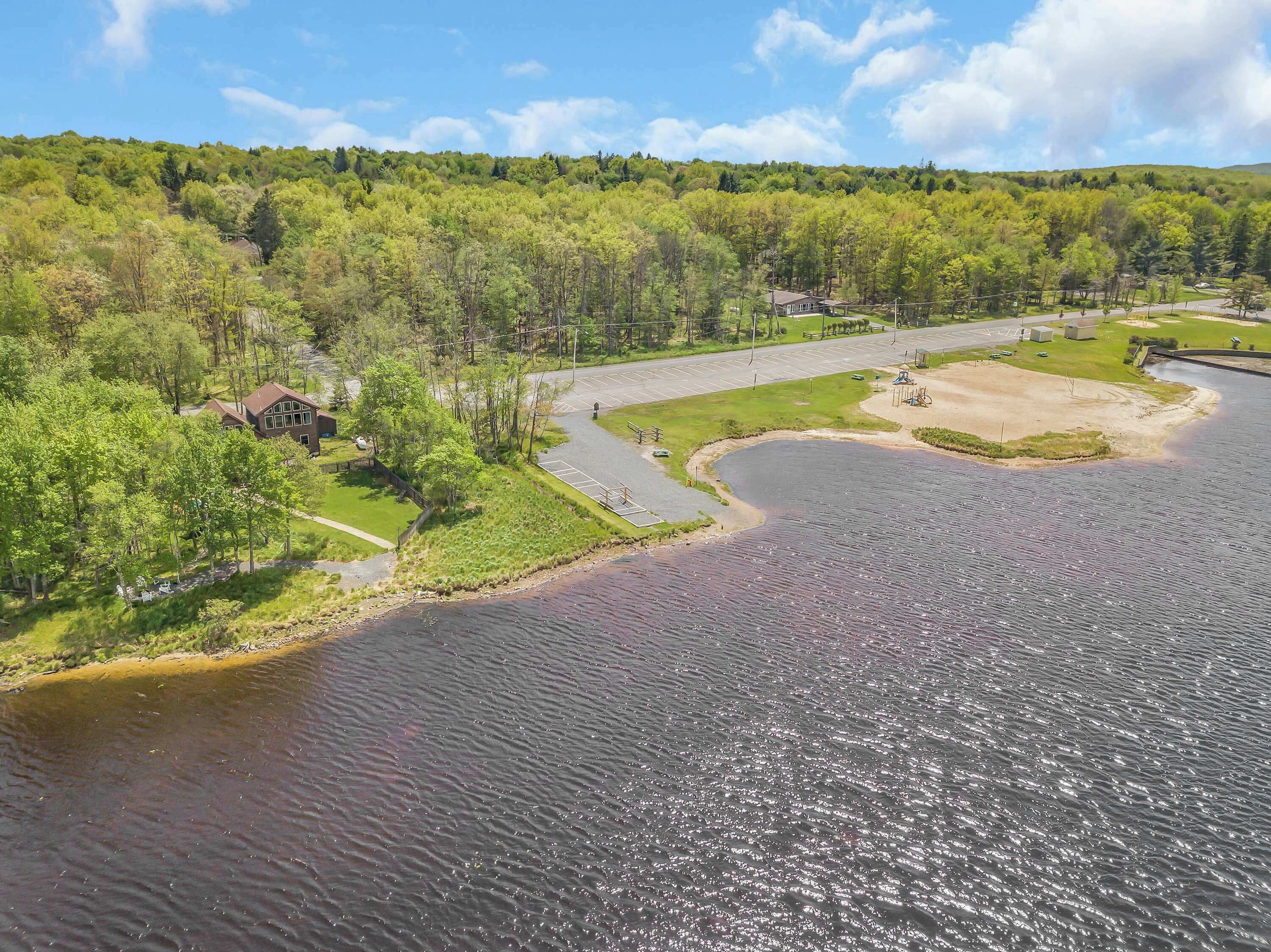 A lakeside property with a house, a parking area, and a grassy area.