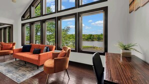 A modern living room with a large window, a sofa, a coffee table, and a chair. - Lakefront Home in the Poconos with Hot Tub! (Albrightsville)