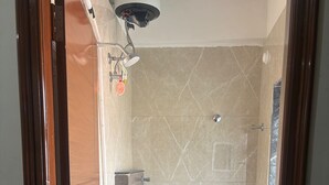 A small, compact bathroom with a toilet, a shower, and a blue bucket.
