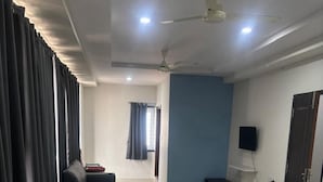 A hotel room with a bed, a sofa, a TV, and a ceiling fan.