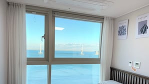A hotel room with a large window offering a view of a bridge and water. There are two wall-mounted air conditioning units and two framed artworks on the wall.