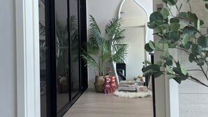 A hallway with a sliding glass door, potted plants, a mirror, and a white rug.