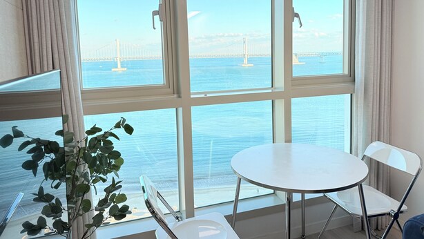 A room with large windows, a round table, a chair, and a potted plant.