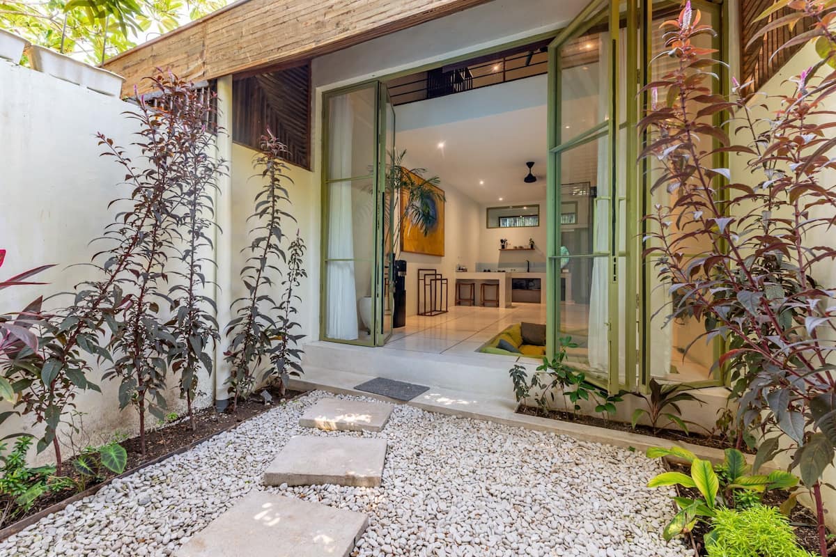 Una casa moderna con un amplio patio, una cocina y un comedor visibles a través de puertas de vidrio.