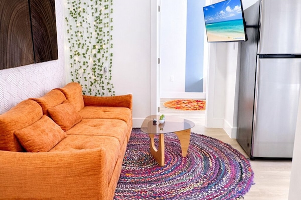 Unwind in the modern living room with orange Sofa, Smart TV, fridge, and rug.