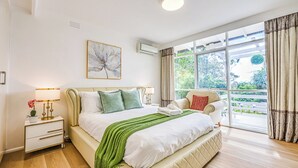 Une chambre à coucher avec un grand lit, une table de chevet, une fenêtre avec des rideaux et une vue sur la verdure.