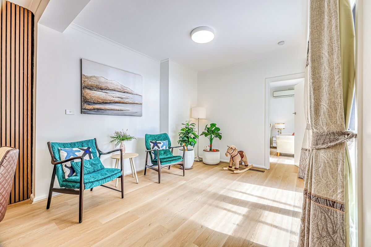 A modern living room with two teal chairs, a wooden rocking horse, and a painting on the wall.