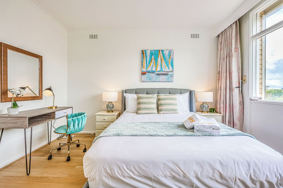 A hotel room with a bed, desk, chair, bedside lamps, and a painting on the wall.