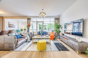 A living room with a sofa, coffee table, ottoman, TV, and large windows. - StayAU Pet-Friendly Prestigious House (Balwyn North)