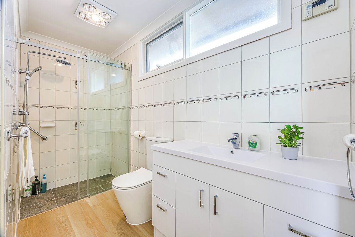 Un baño moderno con cabina de ducha de vidrio, inodoro blanco, lavamanos con espejo y una planta en maceta.
