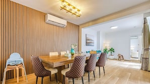 Un coin repas comprenant une table en bois, six chaises rembourrées, une chaise haute pour bébé et un luminaire fixé au plafond.