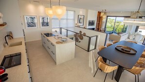 A modern kitchen with a central island, a dining area with wicker chairs, and a view of greenery outside. - Contemporary villa with heated pool, close to the town centre (STE MAXIME)