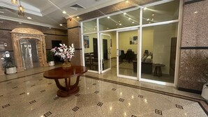 A lobby with a marble floor, a wooden table with a vase of flowers, and a glass door leading to a seating area. - "Samaraham Residency" 3-bedroom fully furnished apartments in Taqah, Salalah! (Taqah)