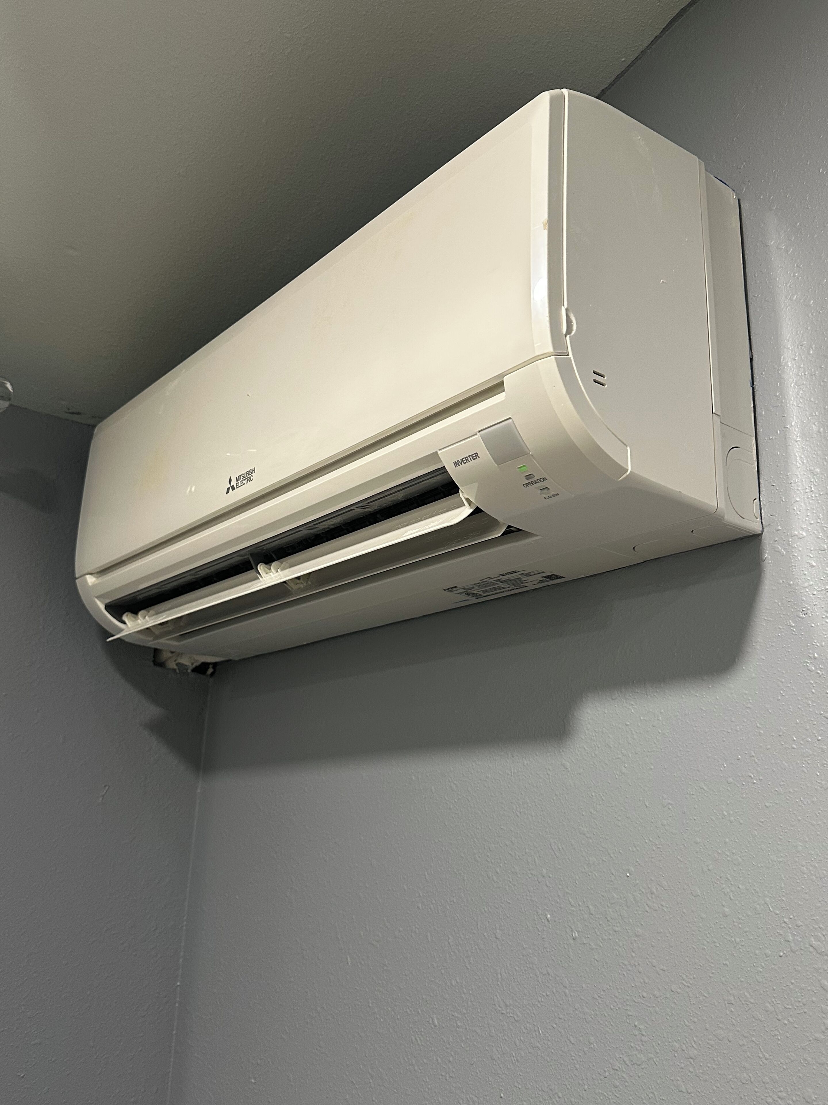 Un aire acondicionado blanco de Mitsubishi Electric montado en una pared gris.