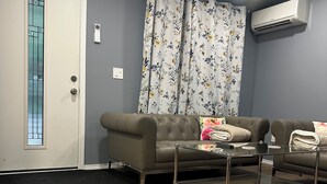 Ein Wohnzimmer mit einer Couch, einem Glastisch und einem gemusterten Vorhang.