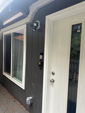 A house exterior with a white door, a garage door, and a window. - Julianna and Allan’s serene green belt view ADU with air conditioning unit. (Everett)