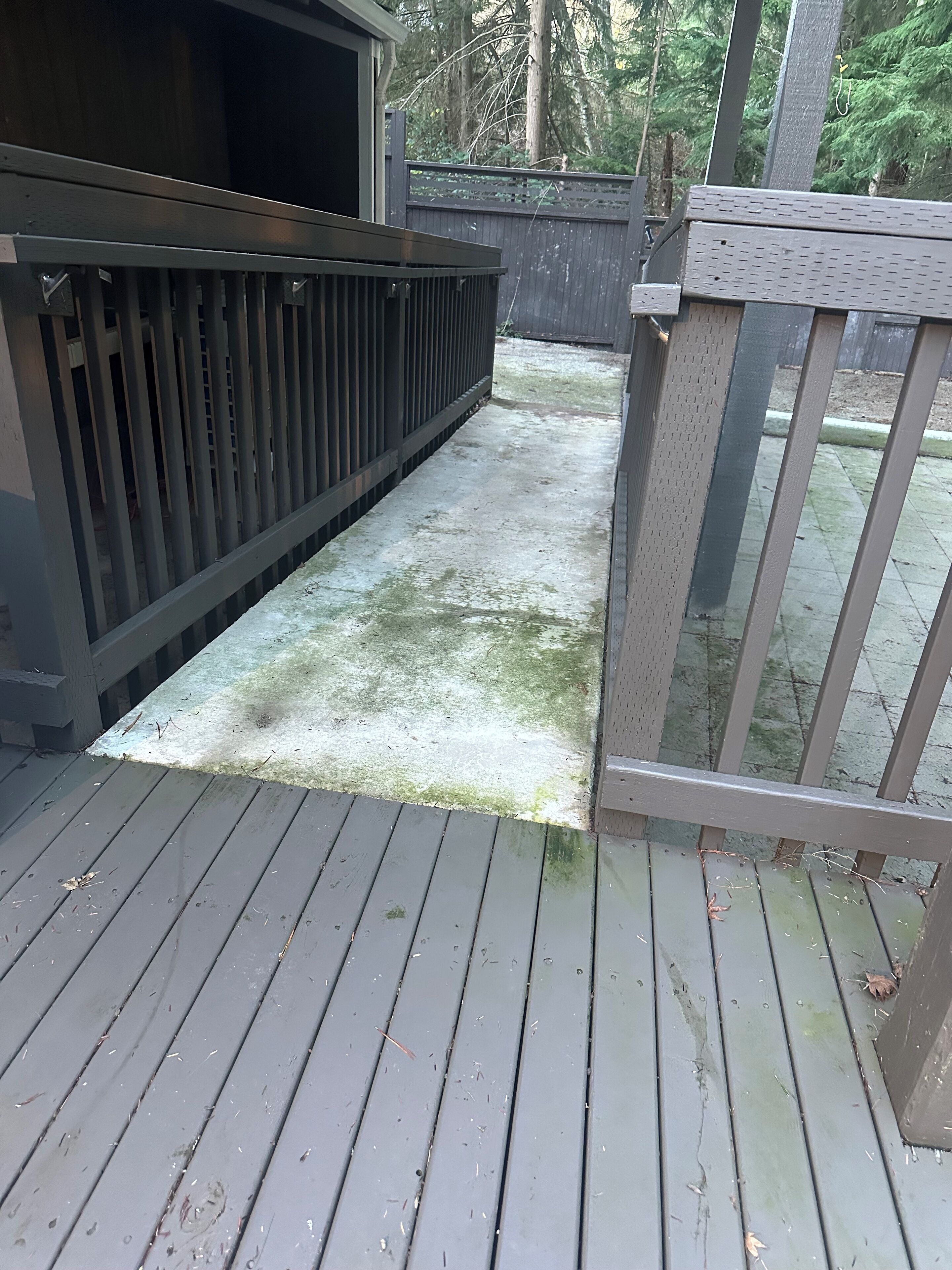Una terraza de madera con baranda de metal y un camino de hormigón.