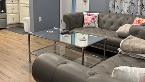 Ein modernes Wohnzimmer mit einem grauen Sofa, einem Glastisch und einer Küchenzeile im Hintergrund.