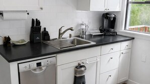 Une cuisine moderne avec des meubles blancs, un lave-vaisselle, une machine à café et une fenêtre donnant sur un beau paysage.