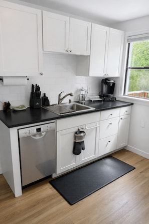 A modern kitchen with white cabinets, a dishwasher, a coffee maker, and a window with a view. - Family‑Friendly 3BR in Seward Park • Walkable • Coffee Shops • Restaurants (Seattle)