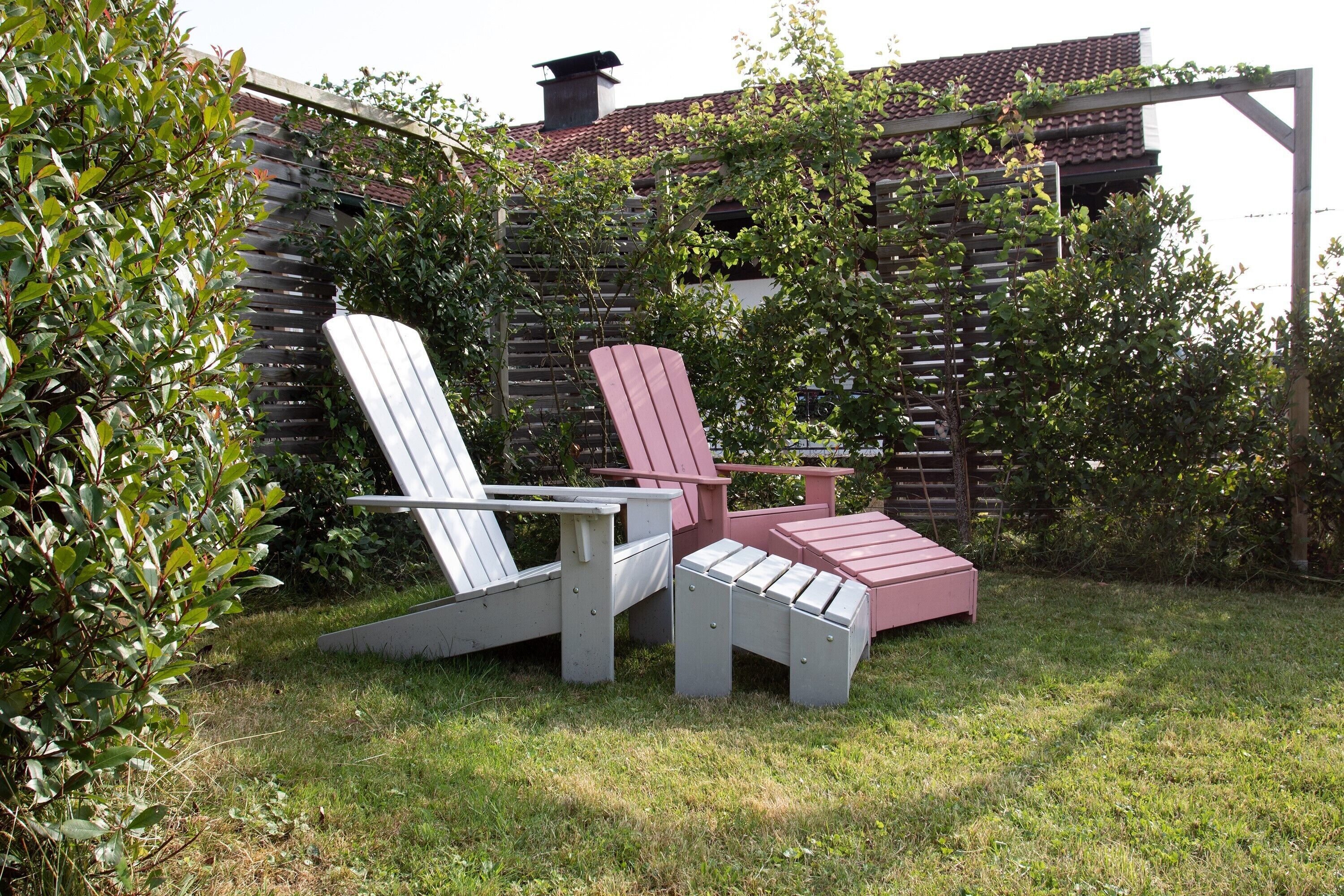 Un jardin agrémenté d’une clôture en bois, d’une pergola en bois et de deux fauteuils Adirondack.