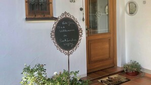 A house entrance with a wooden door, a glass window, a decorative sign, and potted plants. - Vacation apartment with terrace, garden and lake view on the ground floor, for 2 to 3 pers. (Waging am See)